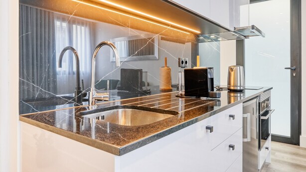 A modern kitchen with a granite countertop, stainless steel appliances, and a large window.
