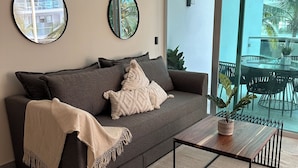 A modern living room with a grey sofa, two wall mirrors, a coffee table, and a view of the outdoors.