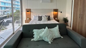 A modern bedroom with a large bed, a ceiling fan, and a view of a building through large windows.