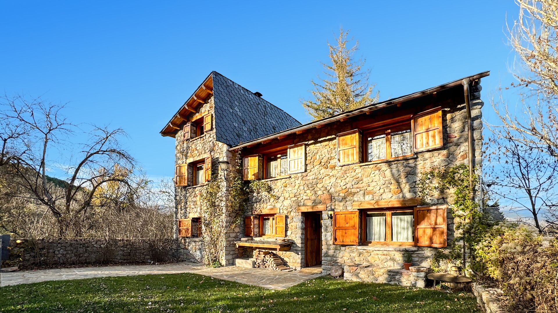 A stone building with a sloped roof, wooden shutters, and a stone staircase leading to the entrance.