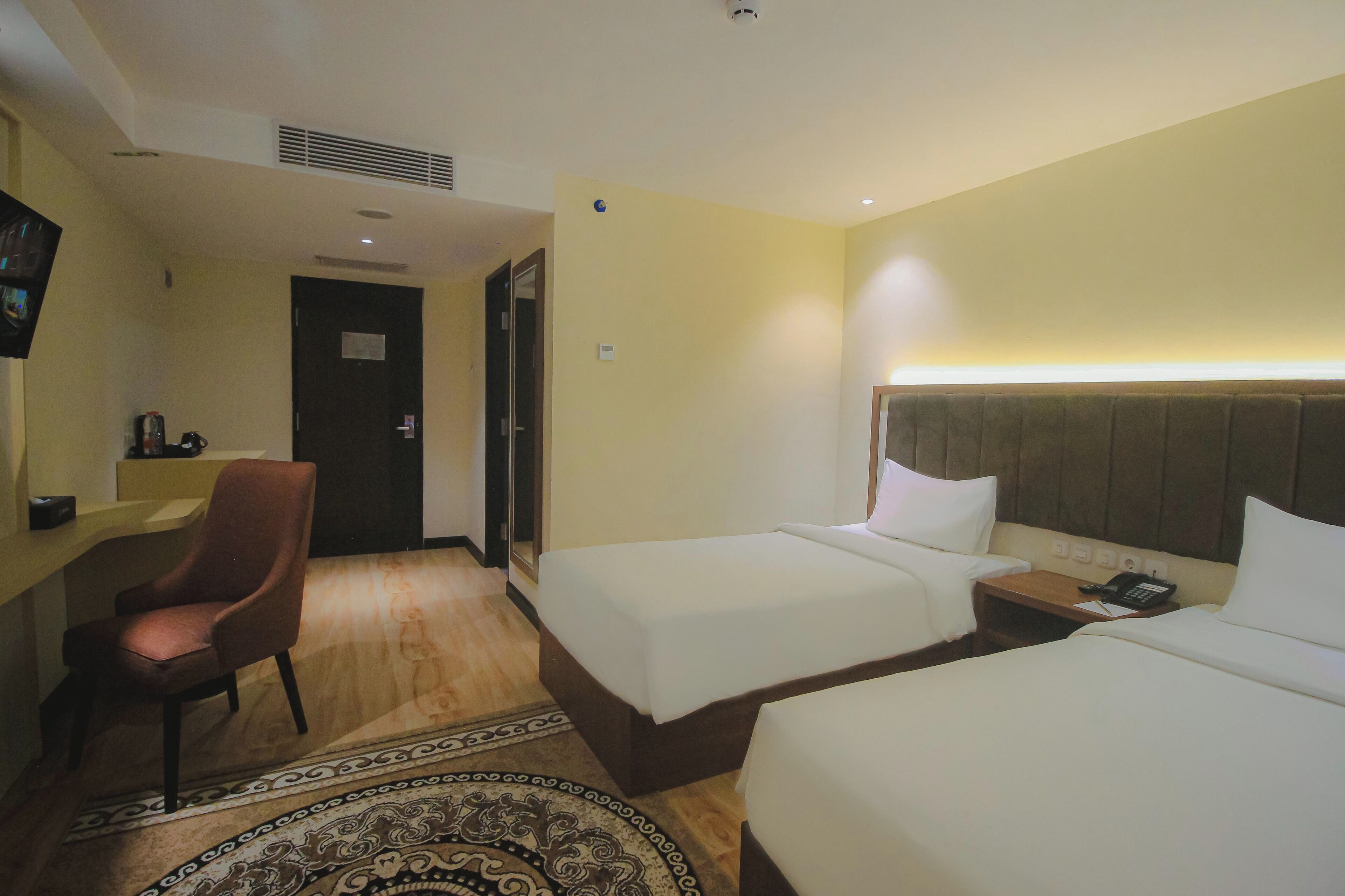 Habitación de hotel con dos camas, una silla, una mesita de noche con teléfono y un televisor en la pared.