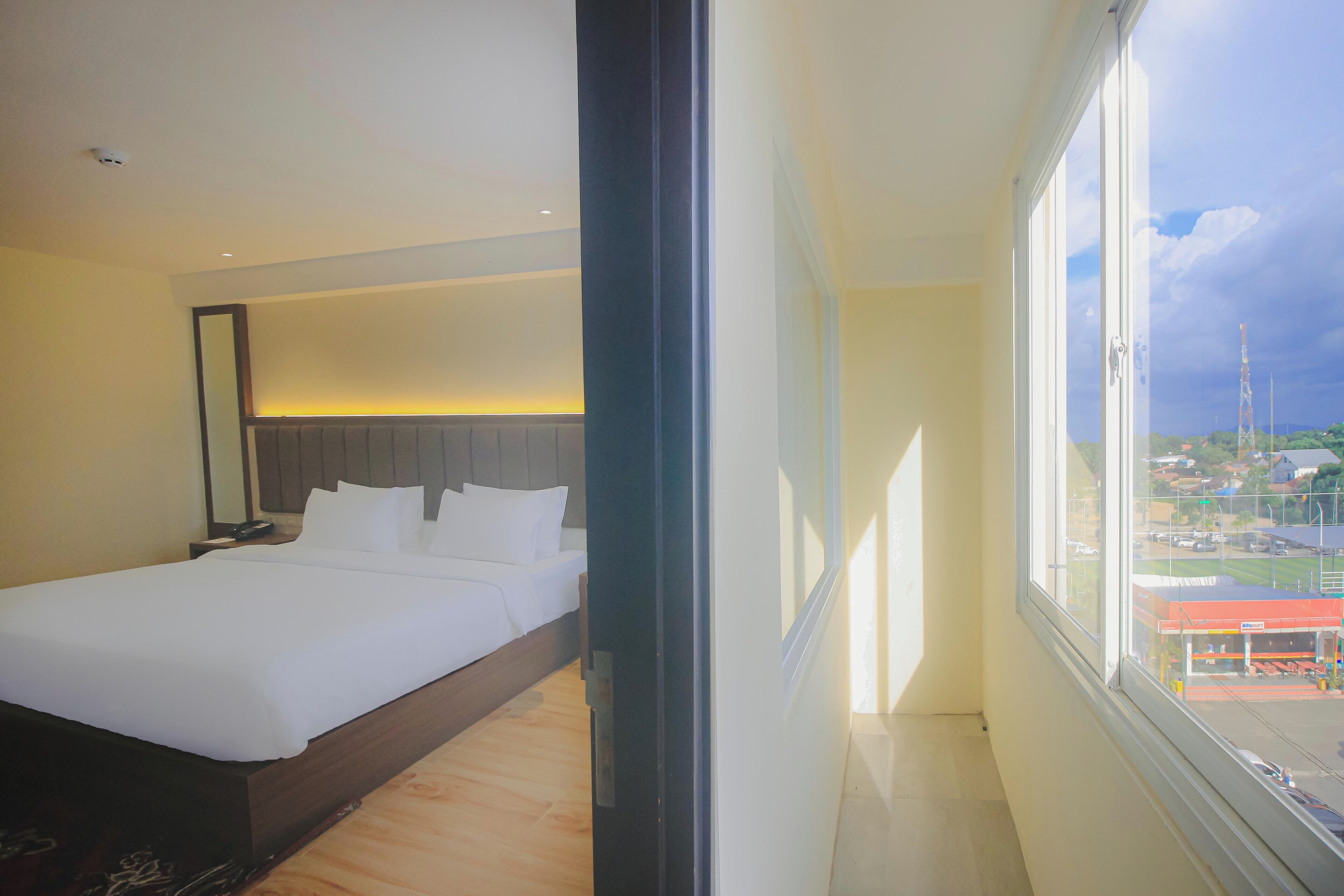 Camera d'albergo con un letto grande, un comodino e vista sulla città attraverso un'ampia finestra.