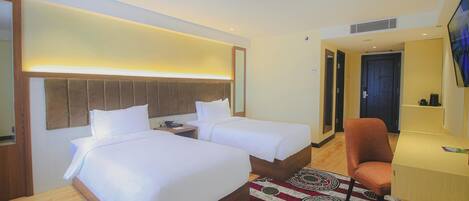 A hotel room with two beds, a desk, a chair, and a television.