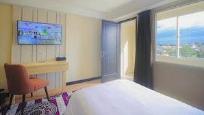 Een hotelkamer met een bed, een bureau, een televisie en een groot raam met uitzicht.