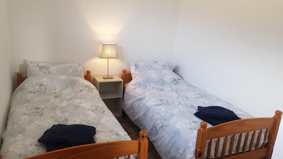 Un dormitorio con dos camas individuales, una mesita de noche con lámpara y cabecero de madera.