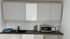A compact kitchen with white cabinets, a microwave, a kettle, and a toaster. - Ldn Studio-Free Parking-15 min to Elizabeth Line (Dagenham)