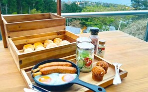 Una mesa de madera con un desayuno que incluye salchichas, huevos, muffins y salsas.