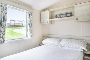 A bedroom with a bed, a window with curtains, a headboard, and a shelf with picture frames.