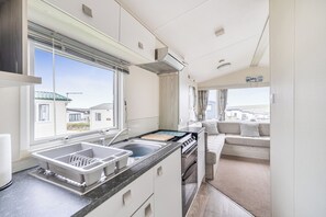 A compact kitchen with a sink, stove, and a dining area with a sofa. - PerranporthCaravan/2bedroom/Tv/GasFire (Perranporth)