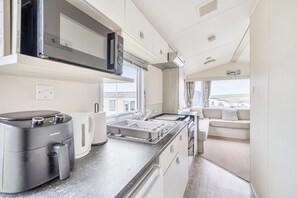 A modern kitchen with a built-in microwave, a coffee maker, and a sink with a drying rack. - PerranporthCaravan/2bedroom/Tv/GasFire (Perranporth)