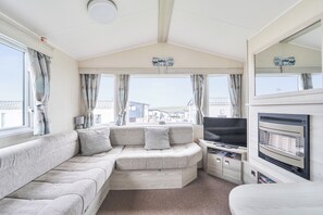 A caravan interior with a sofa, television, and a view of houses through the windows.