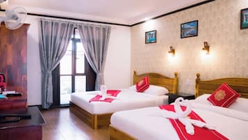A hotel room with two beds, a desk, a chair, a window with curtains, and wall-mounted lights.