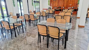 A spacious dining area with multiple tables and chairs, a wooden accent wall, and a television screen.