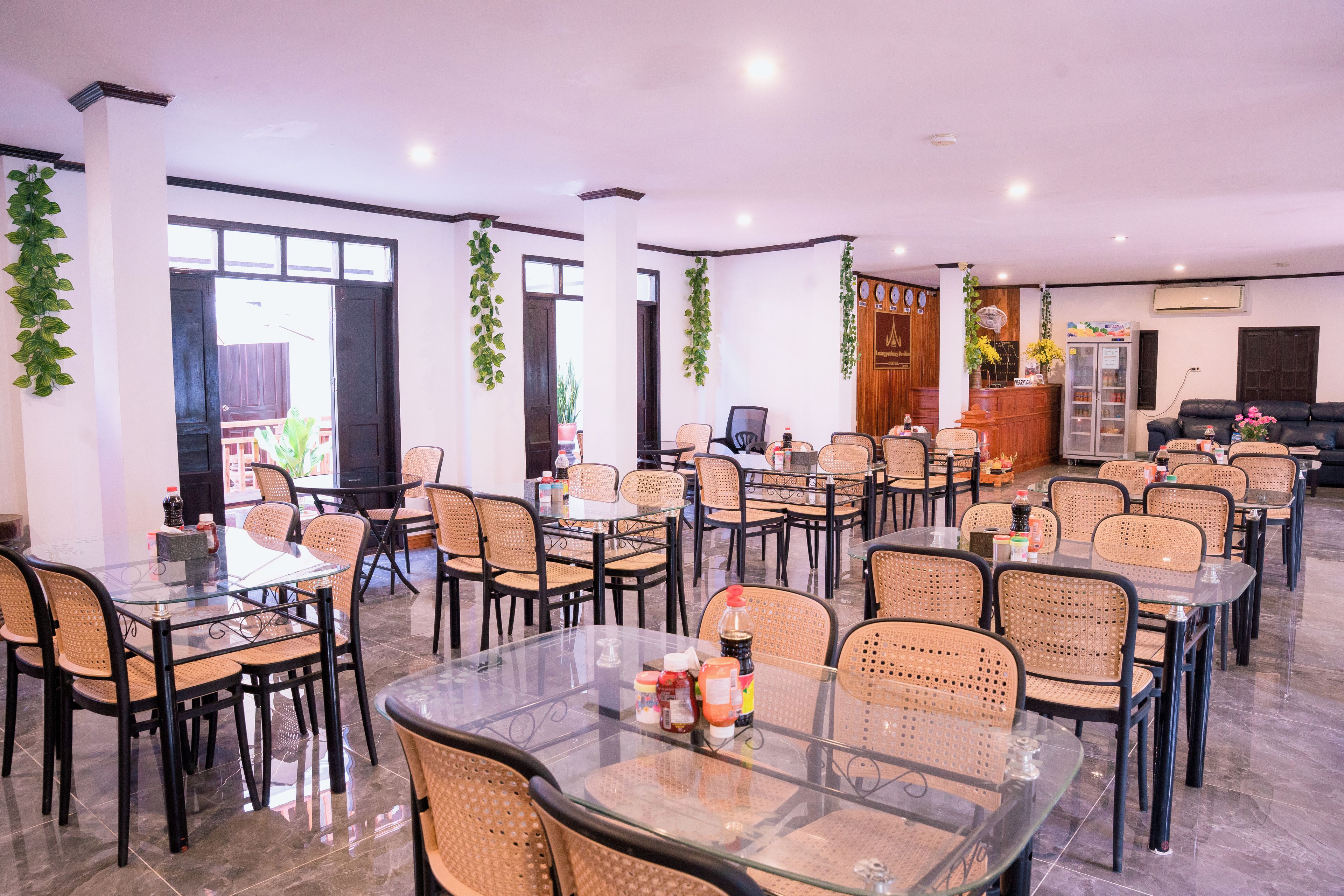 A spacious indoor area with multiple tables and chairs, a reception desk, and decorative plants.