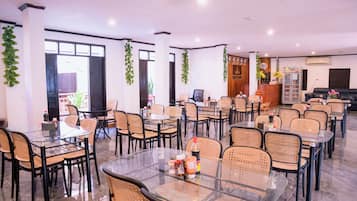 A spacious indoor area with multiple tables and chairs, a reception desk, and decorative plants.
