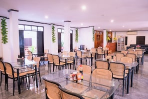 A spacious indoor area with multiple tables and chairs, a reception desk, and decorative plants.
