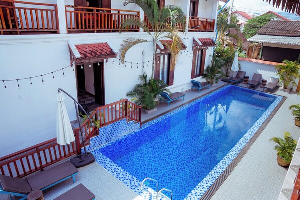 A swimming pool with tiled edges, surrounded by lounge chairs and potted plants. - LuangPrabang Pavilion Hotel & Travel (Luang Prabang)
