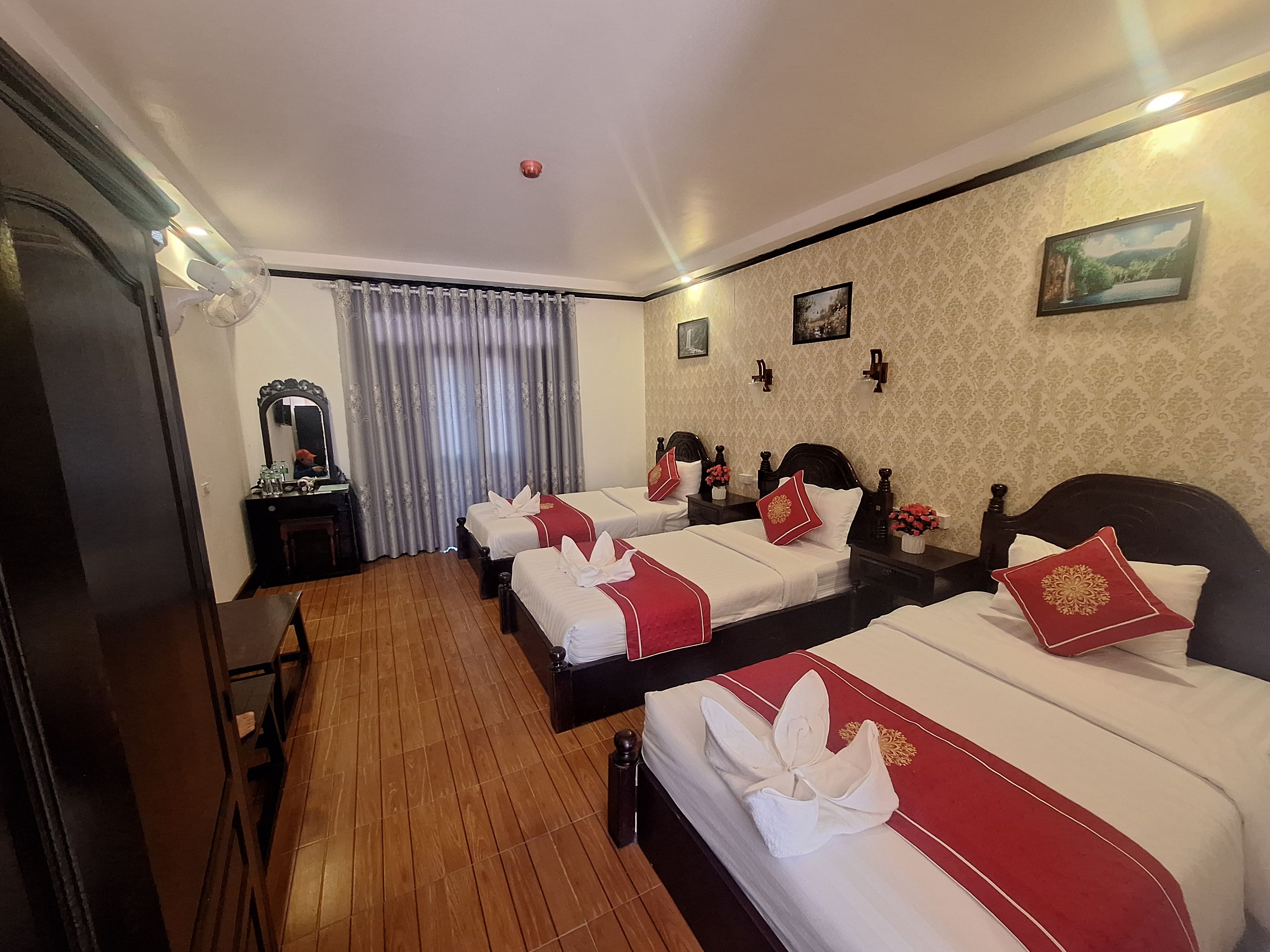 Une chambre d’hôtel avec deux lits, un plancher en bois, un miroir, un bureau et une fenêtre avec des rideaux.