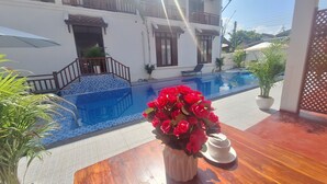 A poolside area with a wooden table, a vase of red flowers, and a white decorative piece. - LuangPrabang Pavilion Hotel & Travel (Luang Prabang)