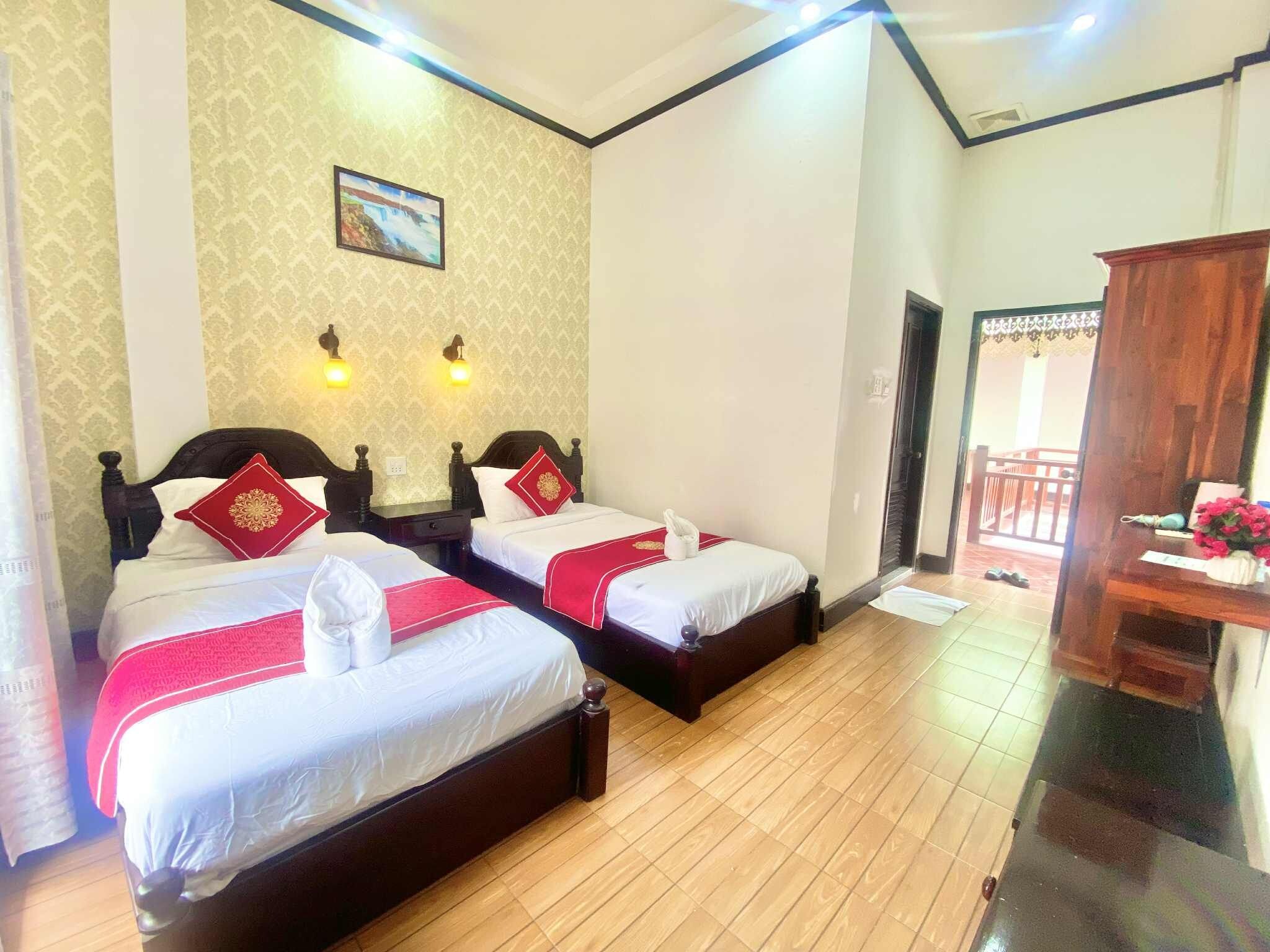 A hotel room with two beds, a wooden floor, a painting on the wall, and a balcony with a railing.