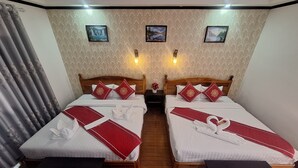 A hotel room with two beds, each with a wooden headboard, white bedding, and red decorative pillows. There are two wall-mounted light fixtures, a nightstand with a vase of flowers, and a wooden bench at each bed. - LuangPrabang Pavilion Hotel & Travel (Luang Prabang)