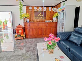 A hotel reception area with a wooden reception desk, a black leather sofa, a marble floor, and a reception sign.
