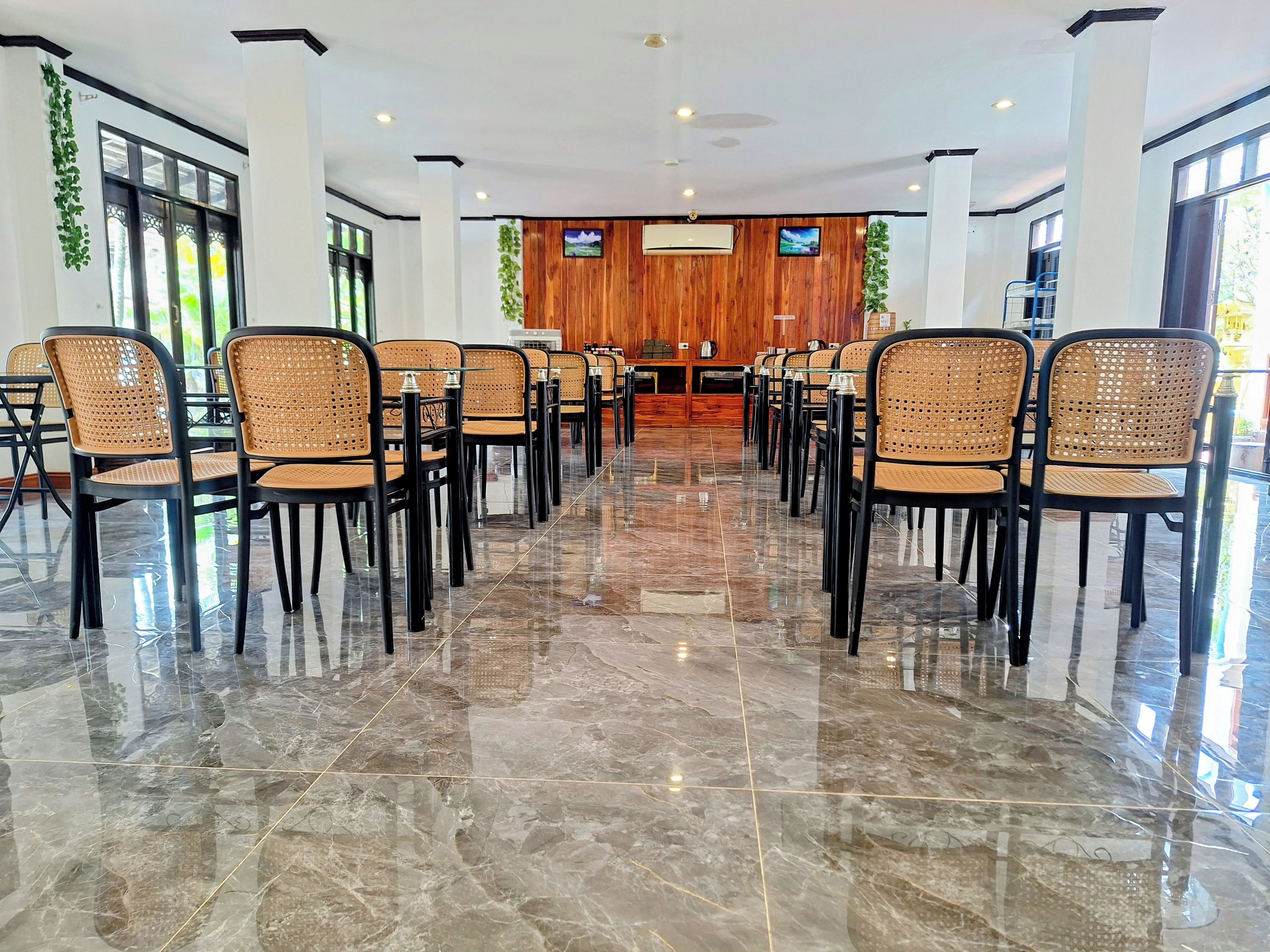 A conference room with a polished marble floor, black chairs with woven seats, and a wooden panel wall with a television.