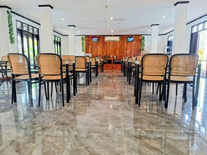 Une salle de conférence dotée d’un sol en marbre poli, de chaises noires à assise tissée et d’un mur en panneaux de bois sur lequel est fixé un téléviseur.