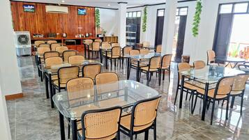 Un vaste espace dédié à la salle à manger, avec des tables en verre et des chaises en osier, des murs lambrissés et un ventilateur de plafond.