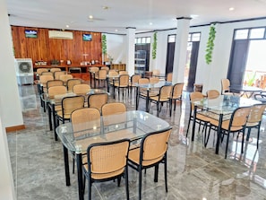 A spacious dining area with glass tables and wicker chairs, wooden panel walls, and a ceiling fan. - LuangPrabang Pavilion Hotel & Travel (Luang Prabang)