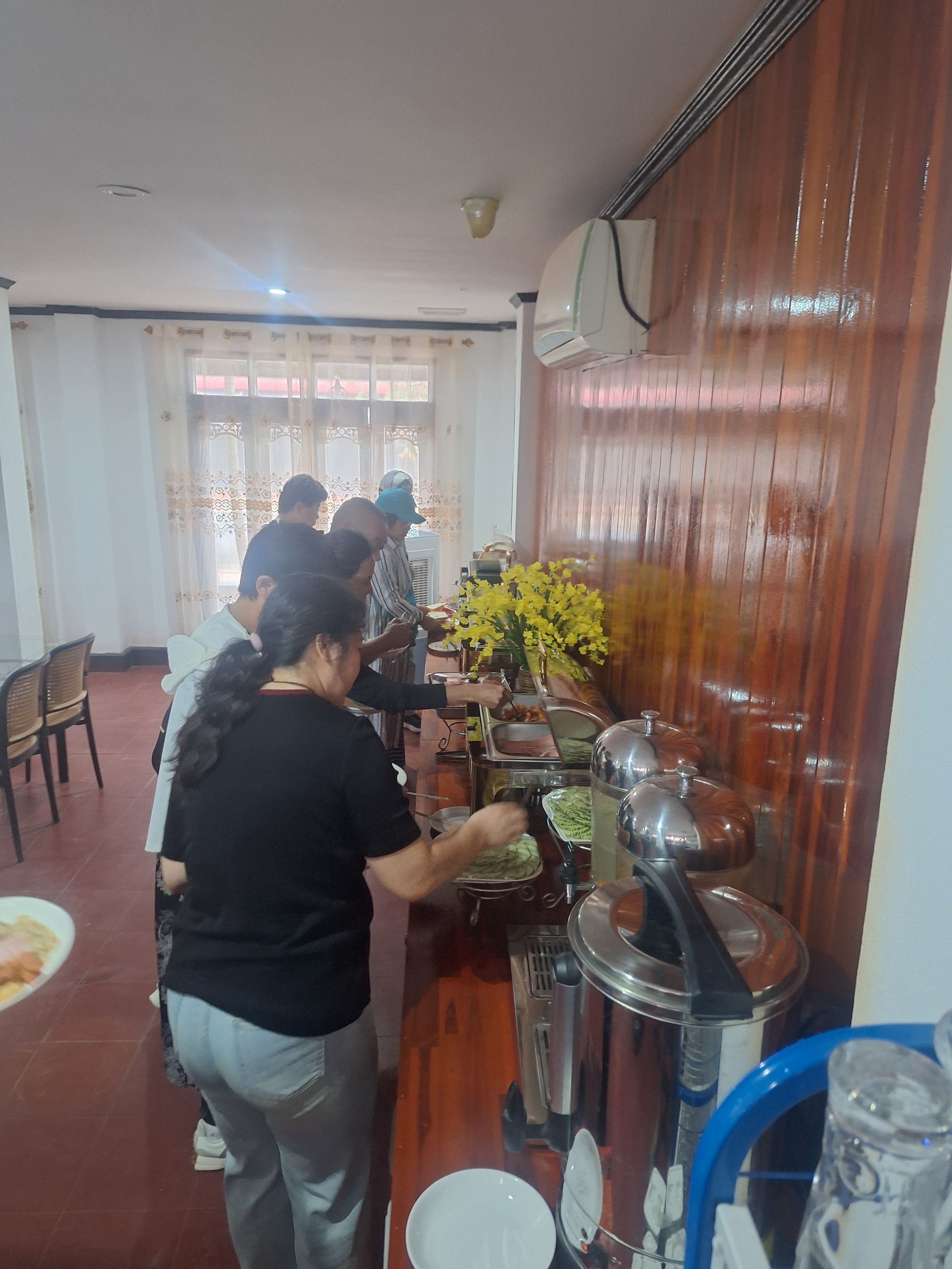 A buffet setup with multiple serving stations, a large vase of yellow flowers, and a water dispenser.