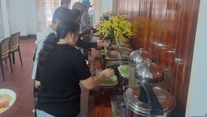 A buffet setup with multiple serving stations, a large vase of yellow flowers, and a water dispenser.