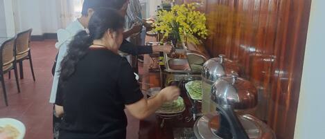 A buffet setup with multiple serving stations, a large vase of yellow flowers, and a water dispenser.