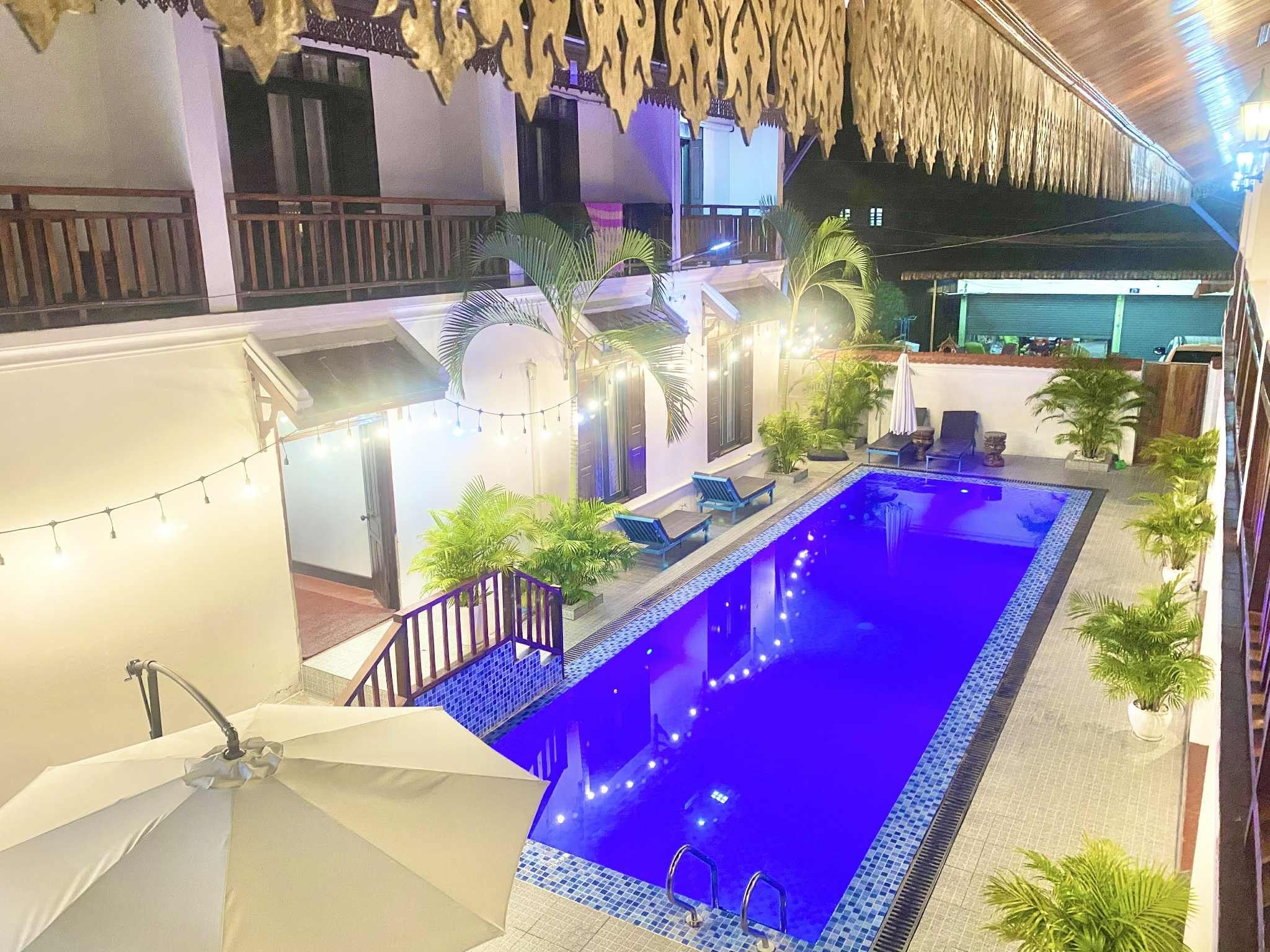 A rooftop pool area with a blue pool, surrounded by potted plants and lounge chairs.