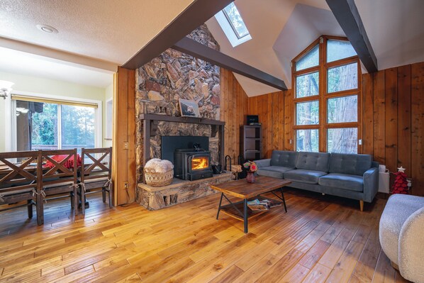 Ein gemütliches Wohnzimmer mit Kamin aus Stein, Holzbalken und einem großen Fenster.