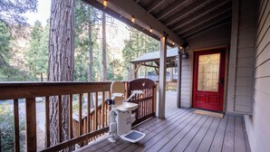 Une terrasse en bois avec une porte rouge, un fauteuil roulant et une vue sur une forêt.