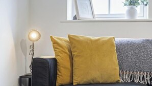 A sofa with two cushions, a floor lamp, and a window with a plant.
