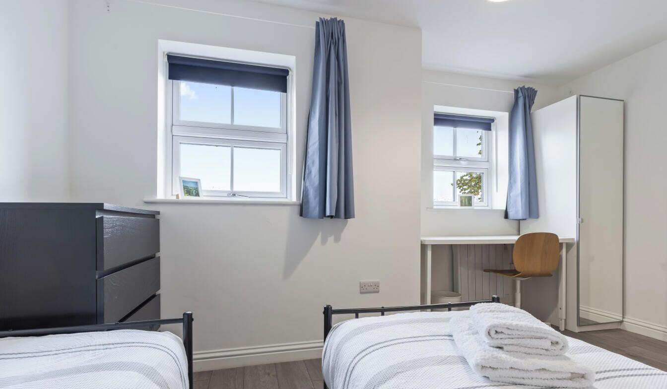 A bedroom with two beds, a desk, a chair, and a wardrobe.