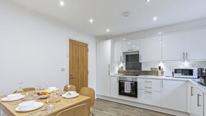 A modern kitchen with white cabinets, a wooden dining table set with plates and glasses, and a microwave.