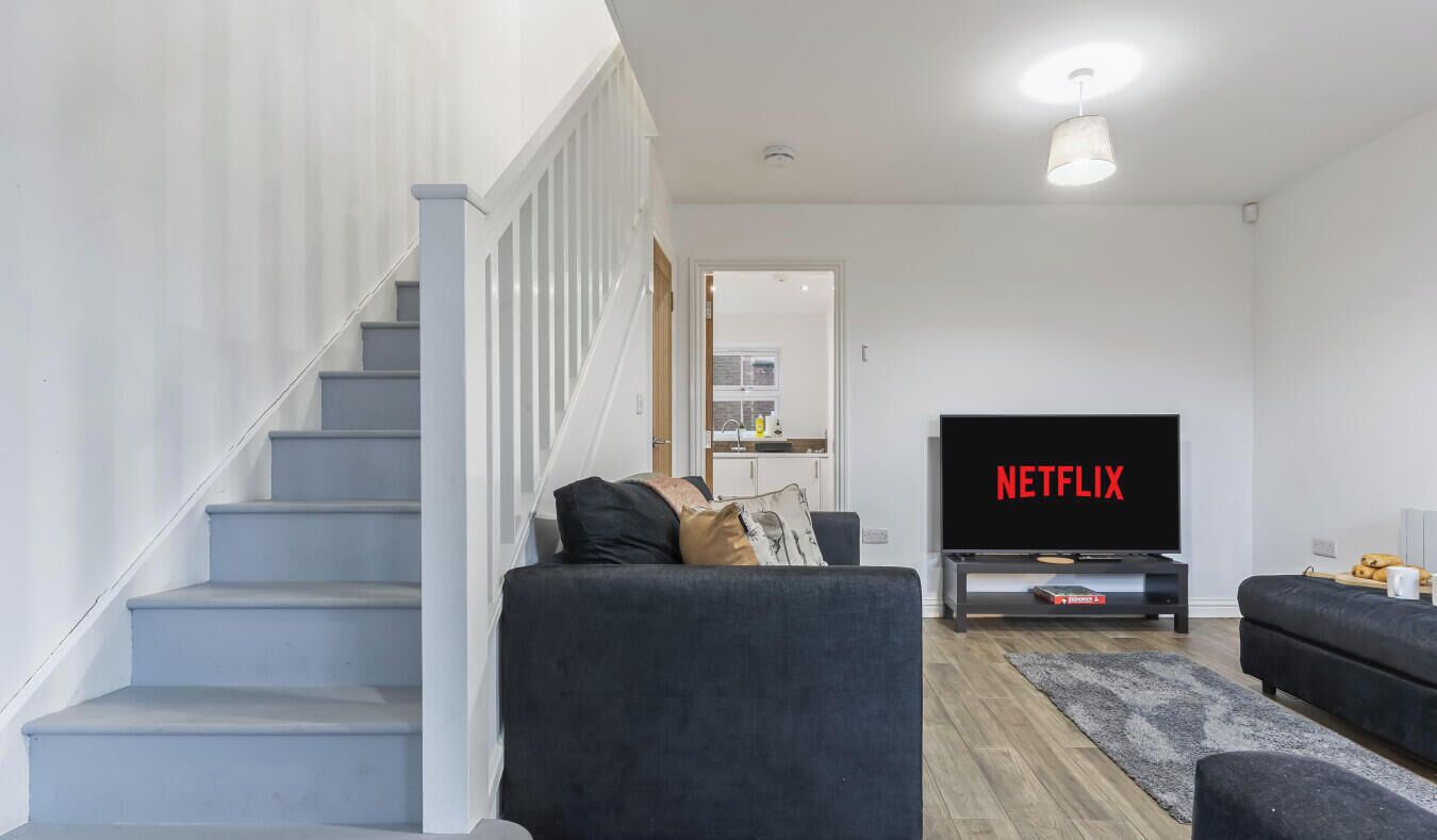 Una sala de estar moderna con una escalera, un televisor de pantalla plana y un sofá.