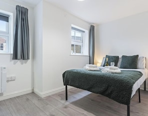 A bedroom with a bed, two windows, a thermostat, and a nightstand. - Lisa's House Leek Parking Close to Alton Towers (Staffordshire)