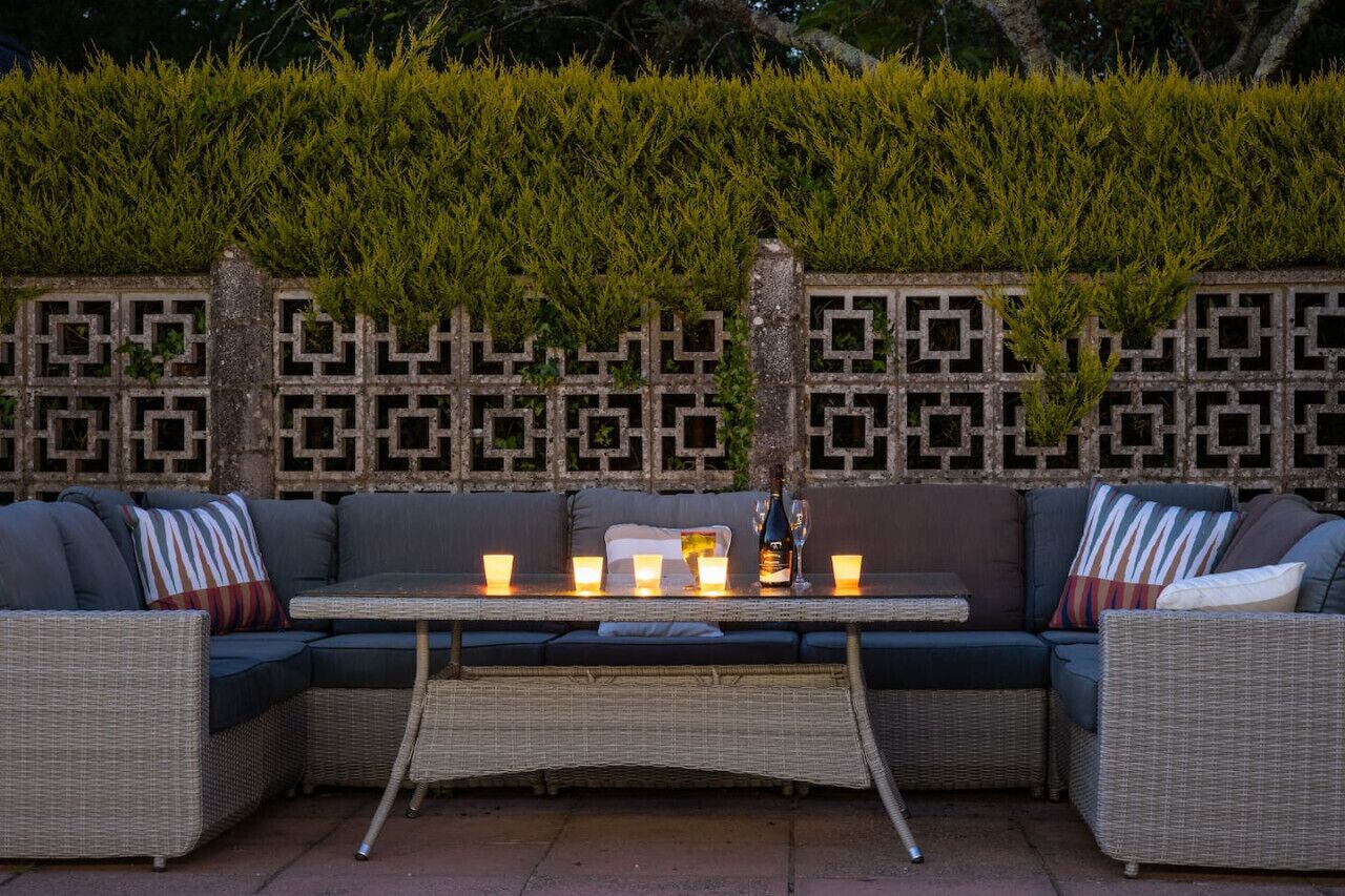 An outdoor seating area with a woven table, cushioned sofas, and a decorative wall with geometric patterns.