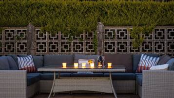 An outdoor seating area with a woven table, cushioned sofas, and a decorative wall with geometric patterns.