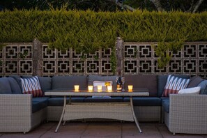 An outdoor seating area with a woven table, cushioned sofas, and a decorative wall with geometric patterns. - Plas Newydd with Swimming Pool (North Wales)