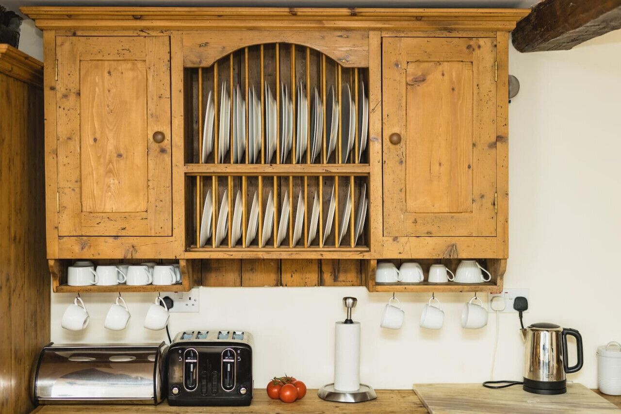 Un buffet en bois, avec des assiettes et des tasses suspendues en dessous.