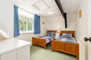 Une chambre à coucher avec deux lits en bois, une commode blanche, une fenêtre avec des rideaux bleus et un puits de lumière.