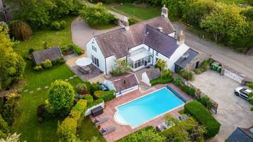 An aerial view of a house with a swimming pool, surrounded by lush greenery and a well-maintained lawn.