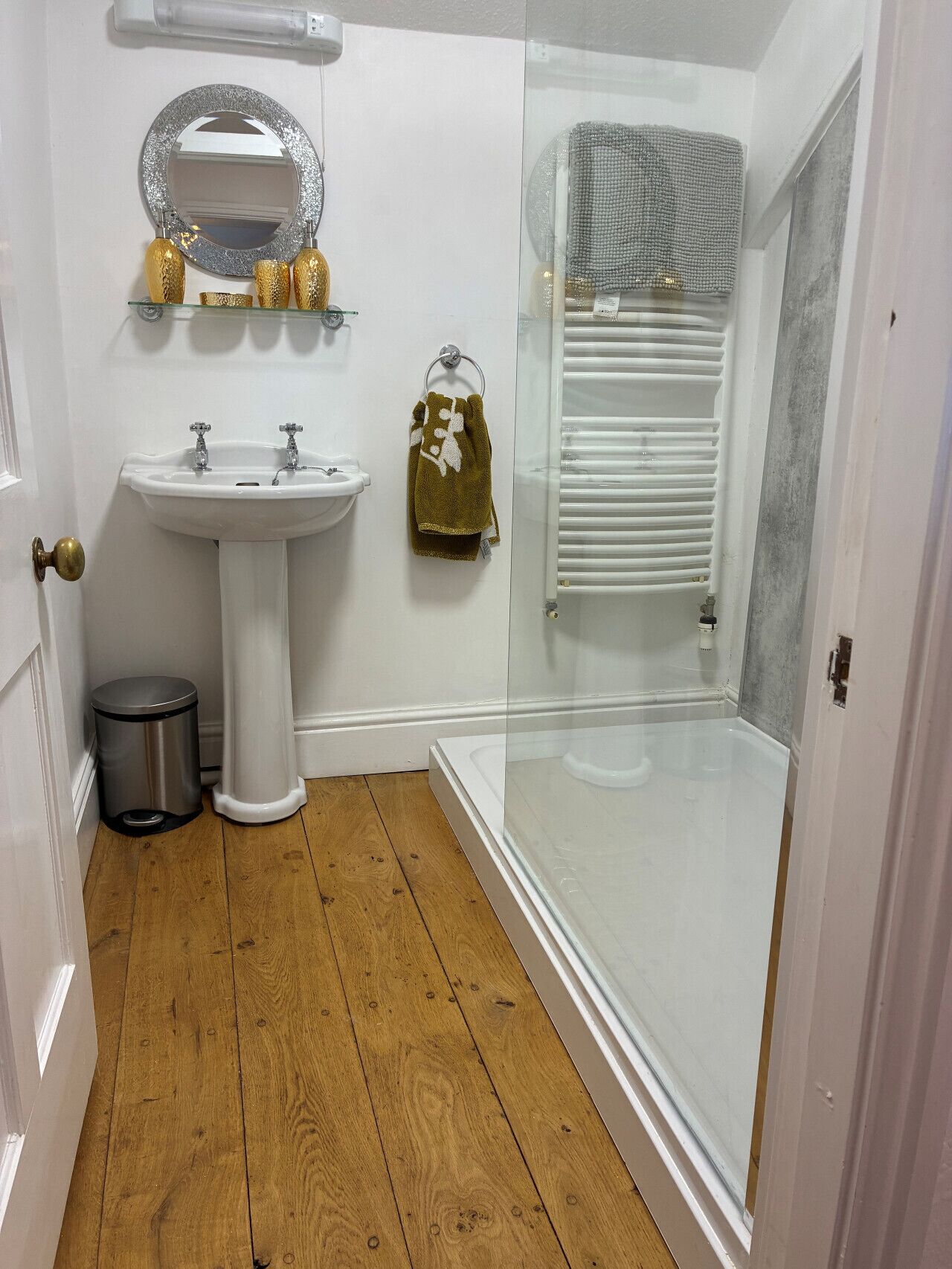 Ein Badezimmer mit weißem Waschbecken, einer Duschkabine aus Glas, einem Handtuchhalter mit Handtuch und einem Mülleimer.