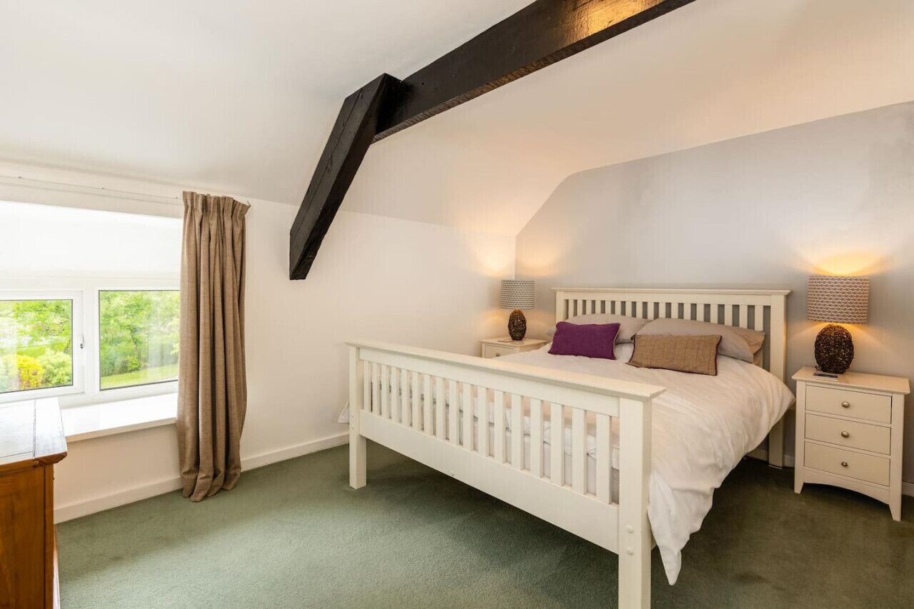 A bedroom with a white bed, two bedside tables, a window with curtains, and a sloped ceiling.