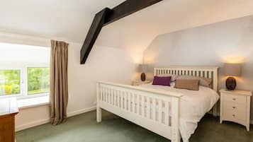 A bedroom with a white bed, two bedside tables, a window with curtains, and a sloped ceiling.